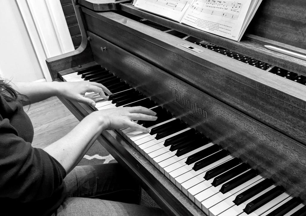 A monochrome picture of Emma playing the piano. Only her hands are visible on the keyboard.